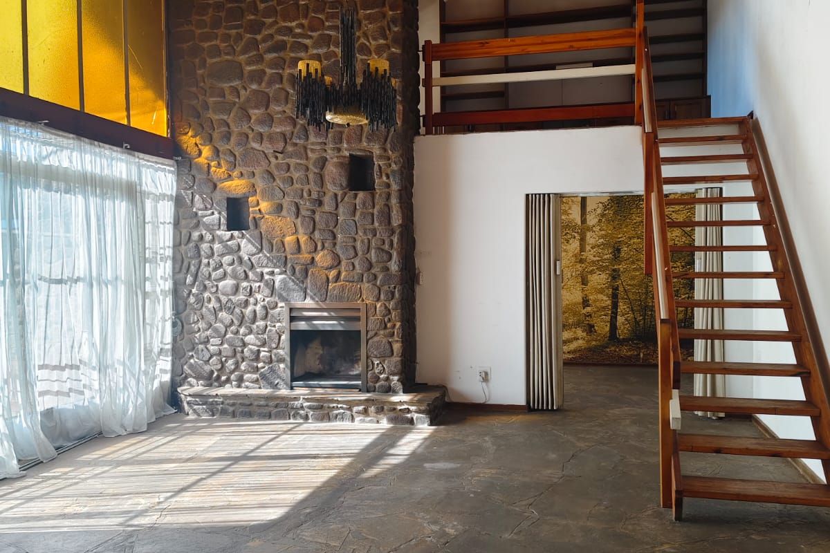 Spacious living room featuring a prominent stone fireplace, timber ceiling, flagstone flooring, and a timber staircase leading to a mezzanine level.