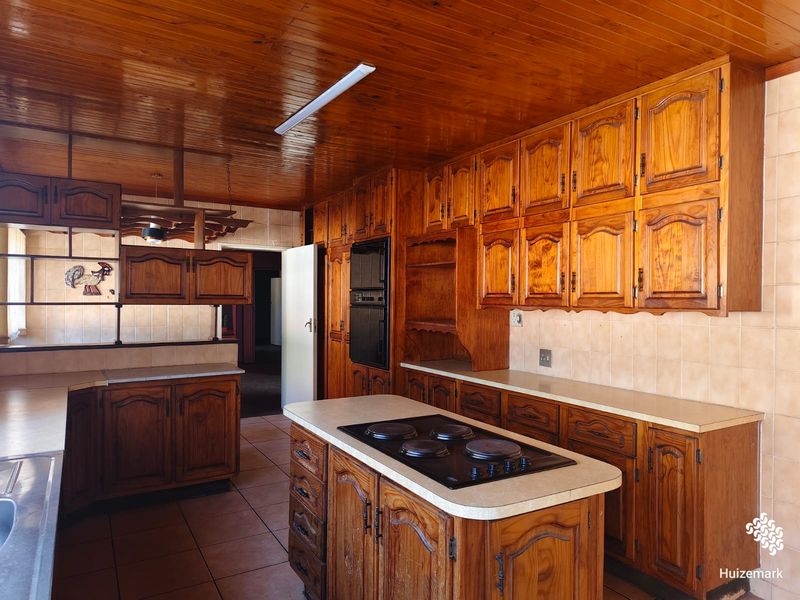 Spacious kitchen featuring extensive wooden cabinetry, a central island with a built-in hob, integrated oven, and tiled finishes throughout.