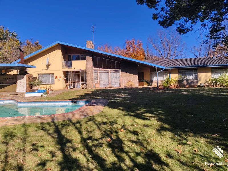 Rear view of the house featuring a swimming pool, stone chimney, and a large garden area with mature trees.