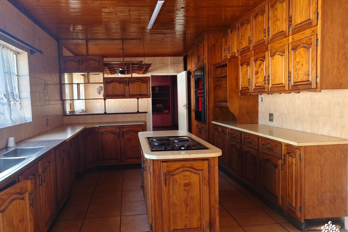 Spacious kitchen featuring extensive wooden cabinetry, a central island with a built-in hob, and tiled flooring, offering a traditional layout with ample storage.