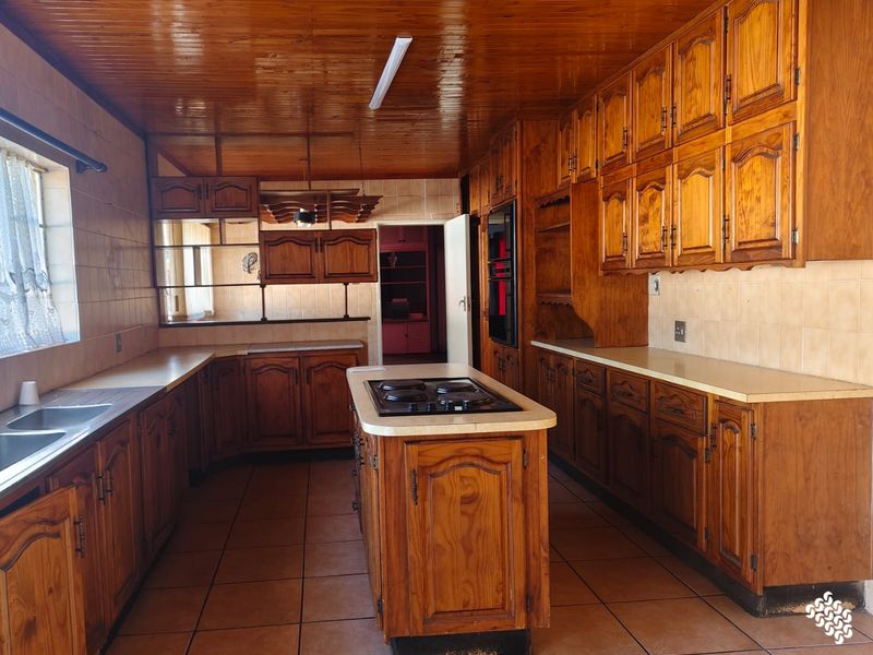 Spacious kitchen featuring extensive wooden cabinetry, a central island with a built-in hob, and tiled flooring, offering a traditional layout with ample storage.