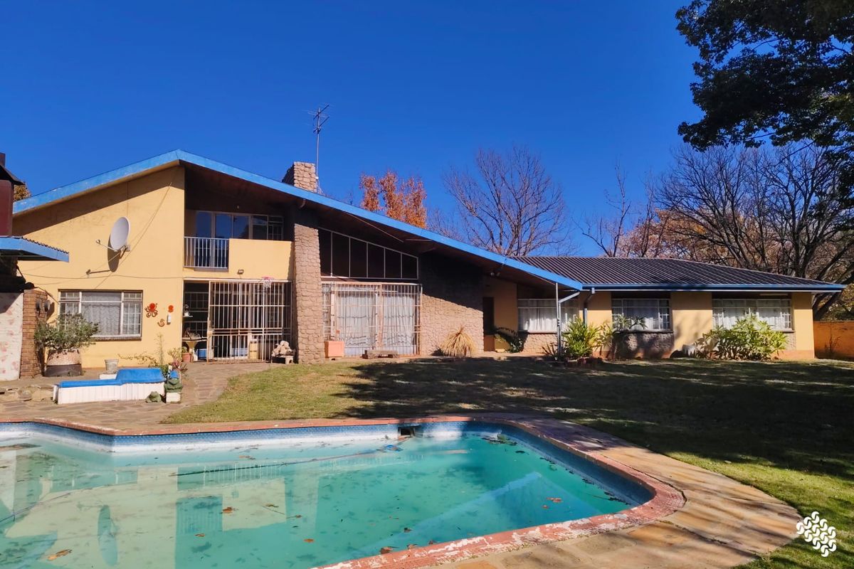 Rear view of the house featuring a swimming pool, stone chimney, and a large garden area with mature trees.