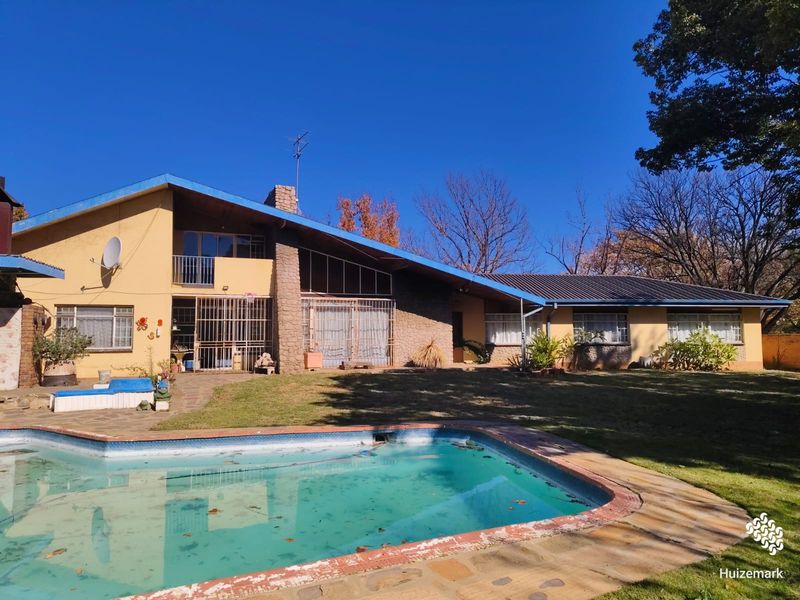 Rear view of the house featuring a swimming pool, stone chimney, and a large garden area with mature trees.