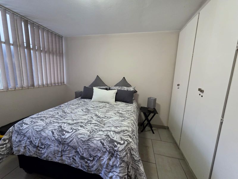 A functional bedroom featuring neutral walls, tiled flooring, built-in cupboards for storage, and vertical window blinds.
