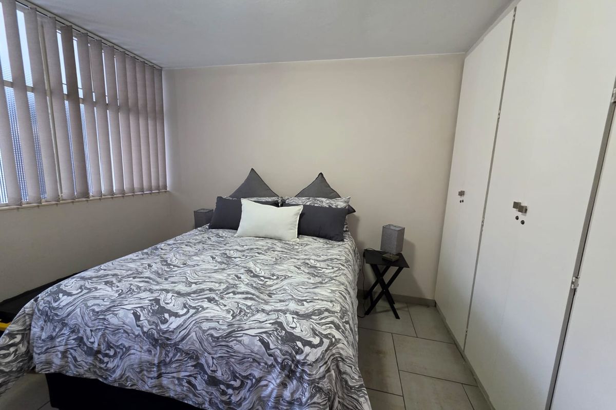 A functional bedroom featuring neutral walls, tiled flooring, built-in cupboards for storage, and vertical window blinds.