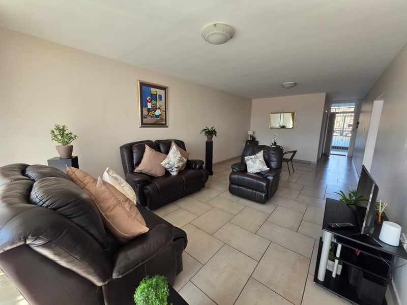 A spacious living room featuring neutral ceramic floor tiles and flush mount lighting, leading towards a secure entrance area.