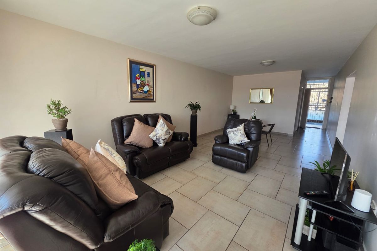A spacious living room featuring neutral ceramic floor tiles and flush mount lighting, leading towards a secure entrance area.