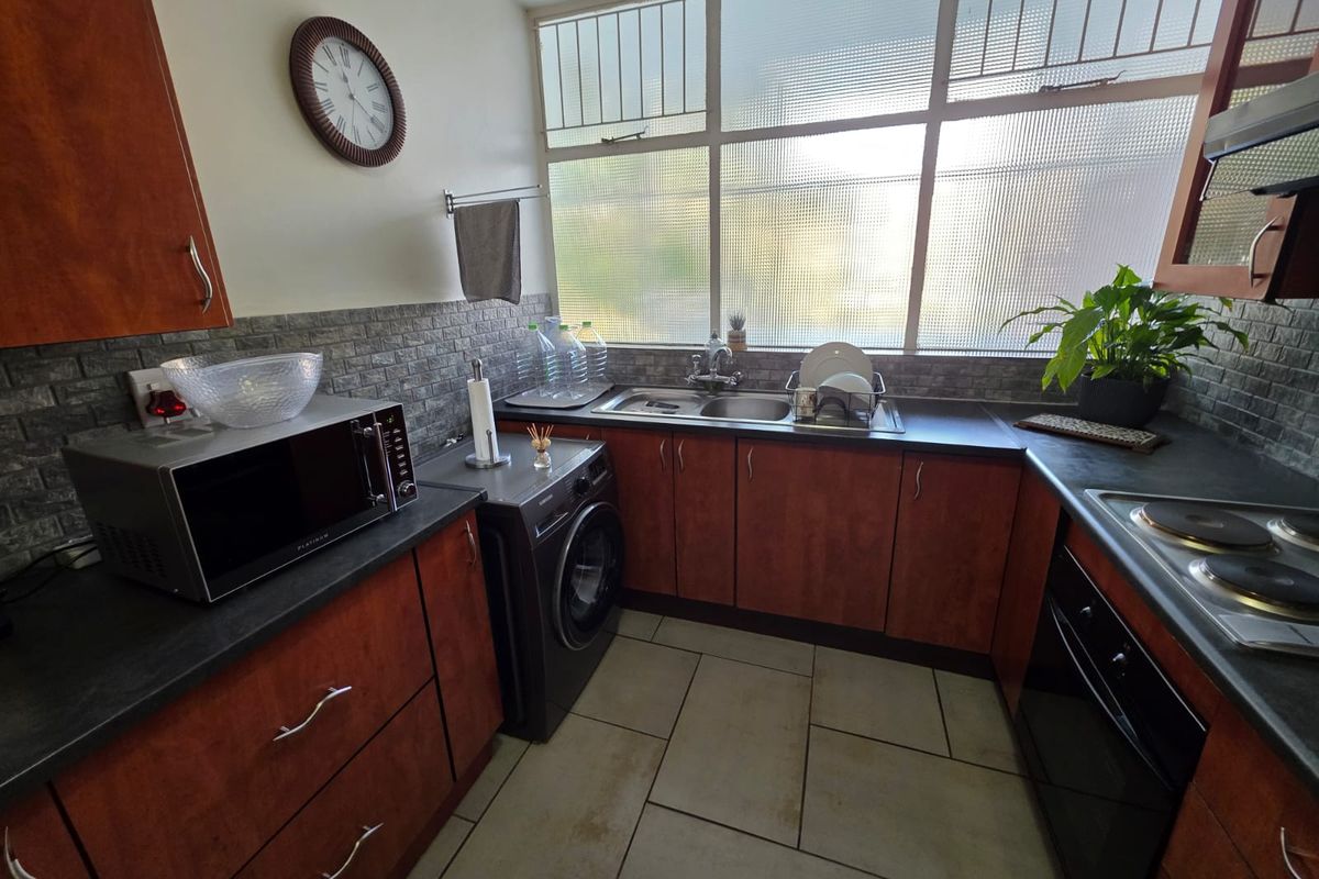 A functional kitchen featuring wood-finish cabinetry, dark countertops, built-in oven and hob, tiled backsplash, and large windows providing natural light.