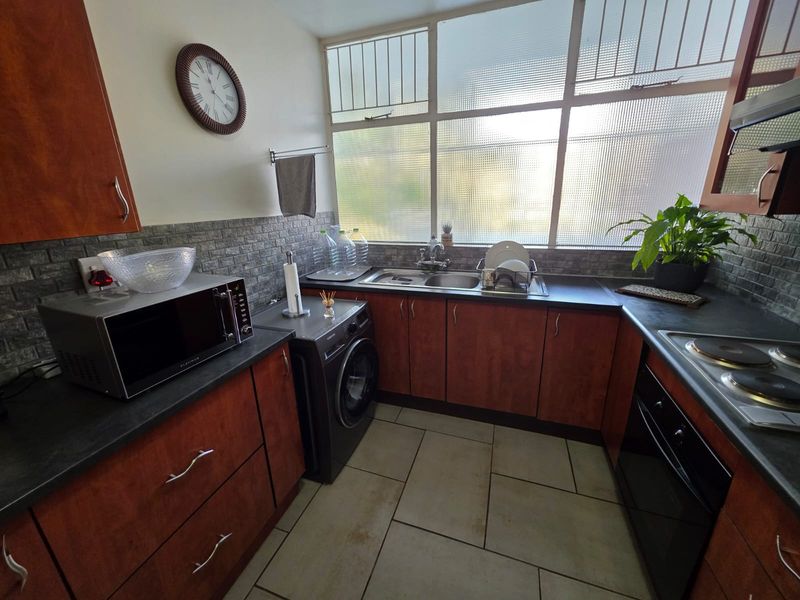 A functional kitchen featuring wood-finish cabinetry, dark countertops, built-in oven and hob, tiled backsplash, and large windows providing natural light.