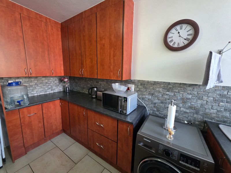 A functional kitchen featuring wood-look cabinetry, stone-style tile backsplash, dark laminate countertops, and ceramic floor tiles.