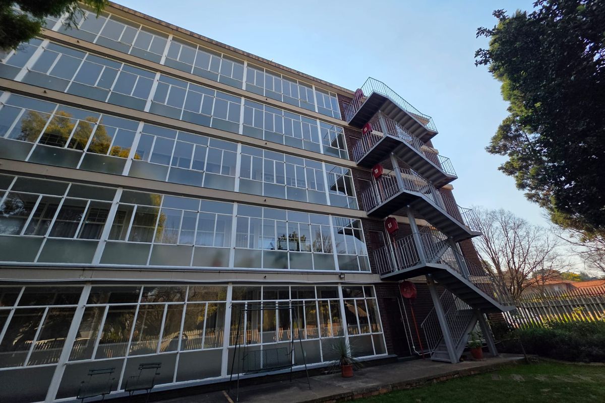 Rear view of a multi-story apartment building featuring a prominent external metal fire escape staircase and extensive glass window facade.