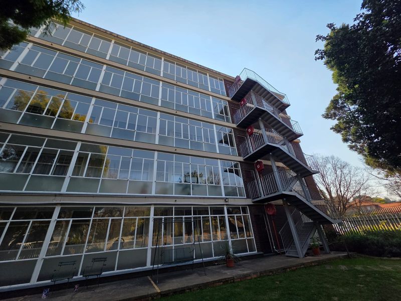 Rear view of a multi-story apartment building featuring a prominent external metal fire escape staircase and extensive glass window facade.