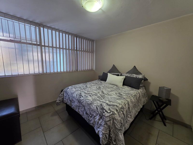 A functional bedroom featuring tiled flooring, vertical window blinds, and a central ceiling light fixture.