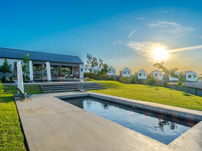 A well-maintained outdoor pool area featuring a concrete deck, landscaped lawn, and tiered steps leading to the main townhouse structure.