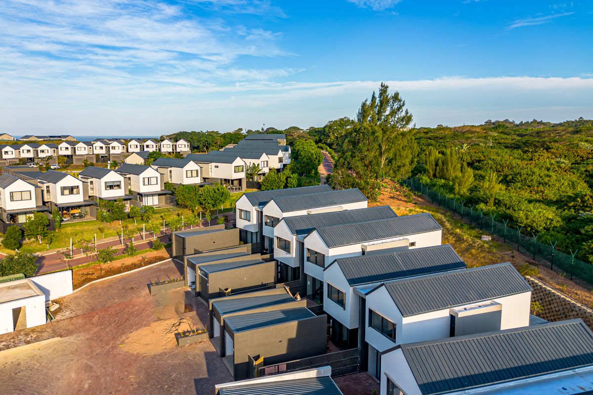 Aerial view of a modern townhouse complex featuring uniform architectural design, metal roofs, and paved access roads within a landscaped estate.