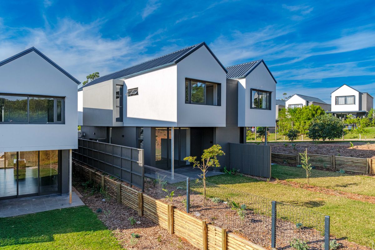 Rear view of a modern townhouse featuring a metal roof, paved patio area, and private garden with timber fencing.