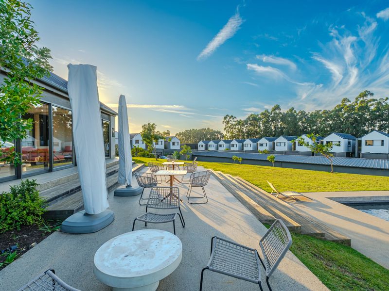 Spacious outdoor patio area featuring concrete paving, timber decking, and direct access to a swimming pool and landscaped garden.