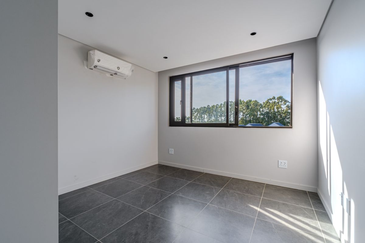 A bright, modern, and empty bedroom featuring neutral walls, large sliding windows, tiled flooring, and a wall-mounted air conditioning unit.
