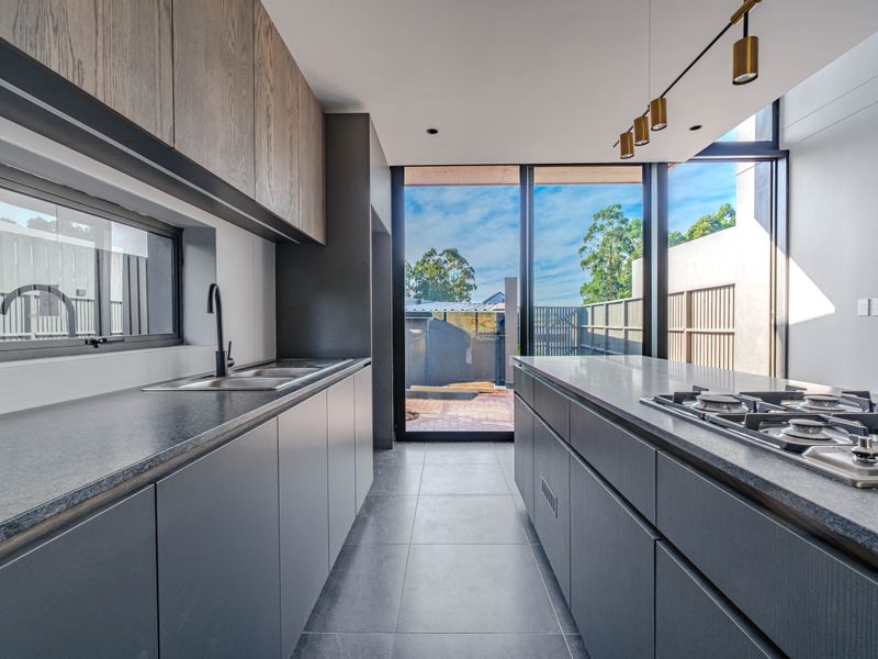 Modern kitchen featuring sleek dark cabinetry, stone countertops, a gas cooktop, and large windows providing natural light and access to the outdoor area.