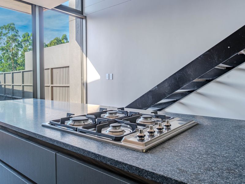 Modern kitchen area featuring a built-in gas hob, stone countertops, and sleek cabinetry, adjacent to an open staircase and large glass doors.