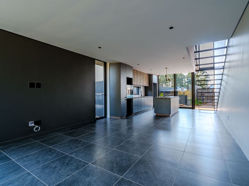 Modern open-plan living and kitchen area featuring sleek cabinetry, a central island, tiled floors, and a striking floating staircase leading to the upper level.