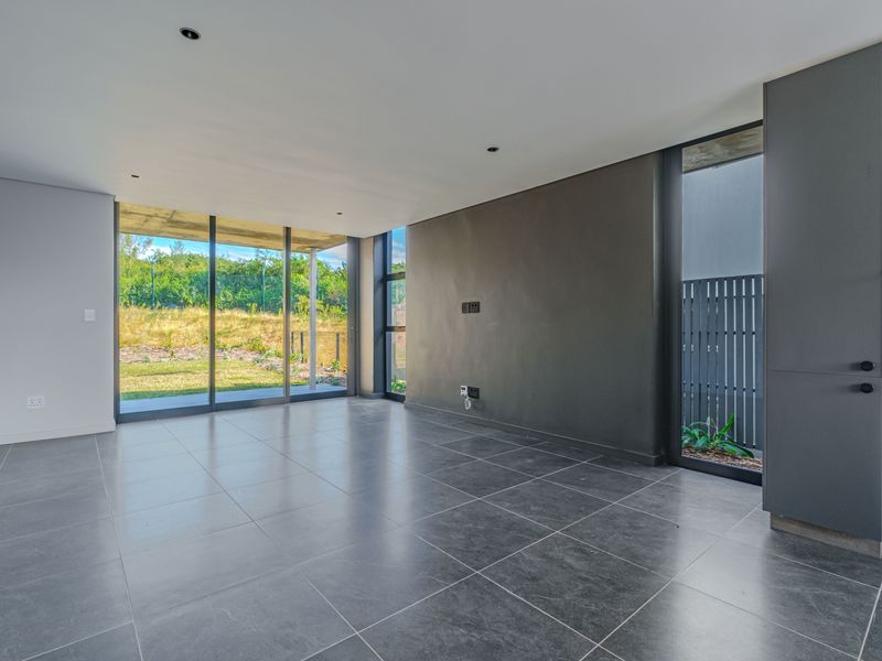 Modern open-plan living area featuring large format floor tiles, recessed lighting, and expansive sliding glass doors leading to a private garden.