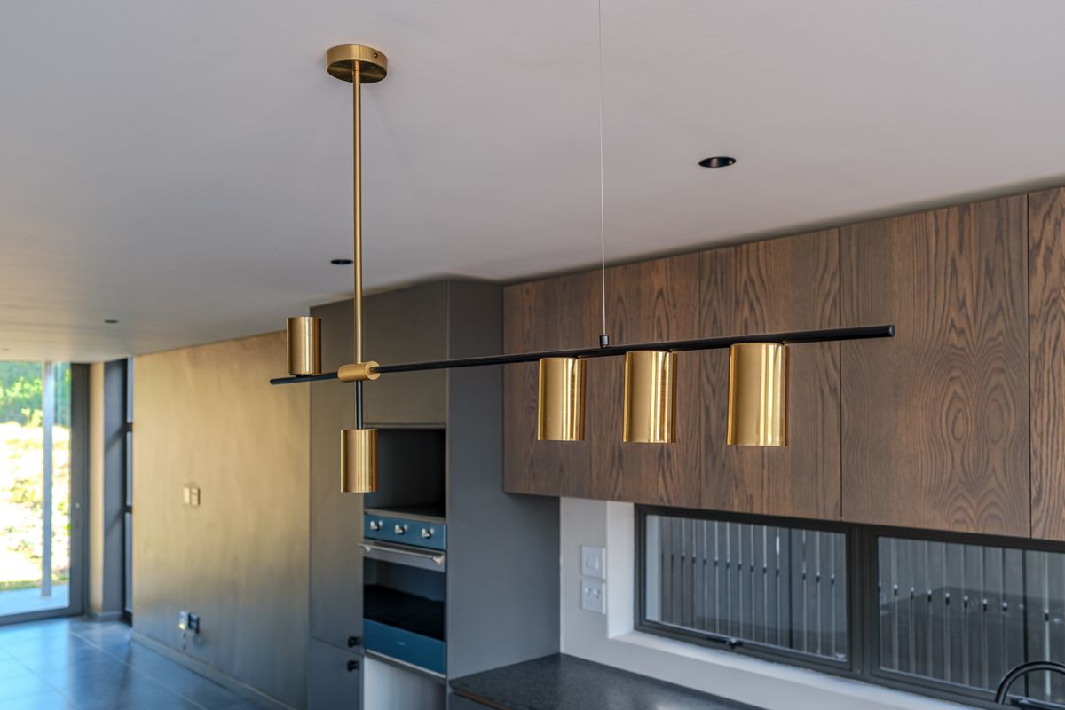 Modern kitchen featuring dark wood cabinetry, built-in oven, stone countertops, and contemporary gold pendant lighting in an open-plan layout.