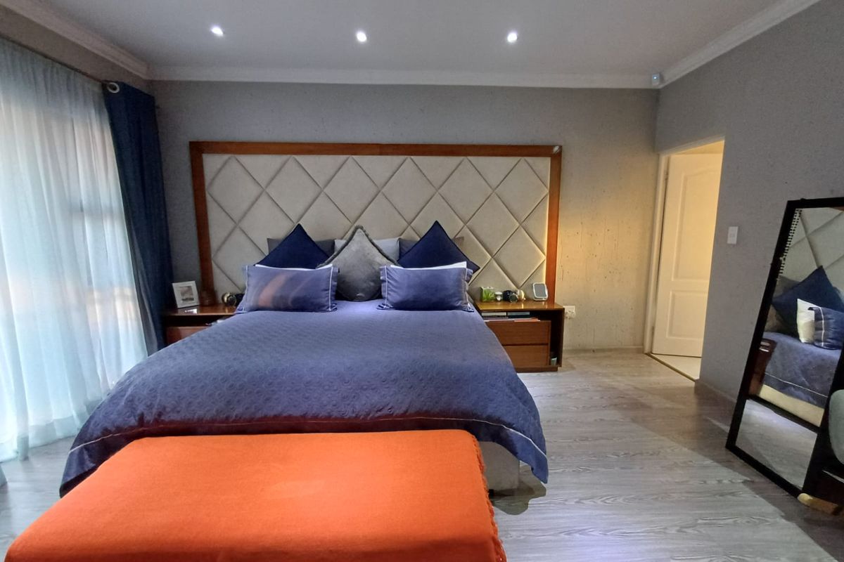 Spacious bedroom featuring modern laminate flooring, recessed downlighting, and a large custom upholstered headboard.