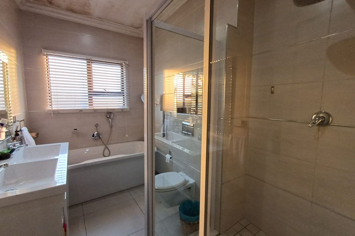 Modern bathroom featuring a double vanity, freestanding bathtub, and glass-enclosed shower, though the ceiling shows signs of significant water damage.