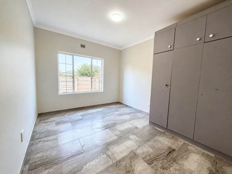 A clean, empty bedroom featuring modern grey tiled flooring and built-in cupboards, offering a neutral canvas for personalization.