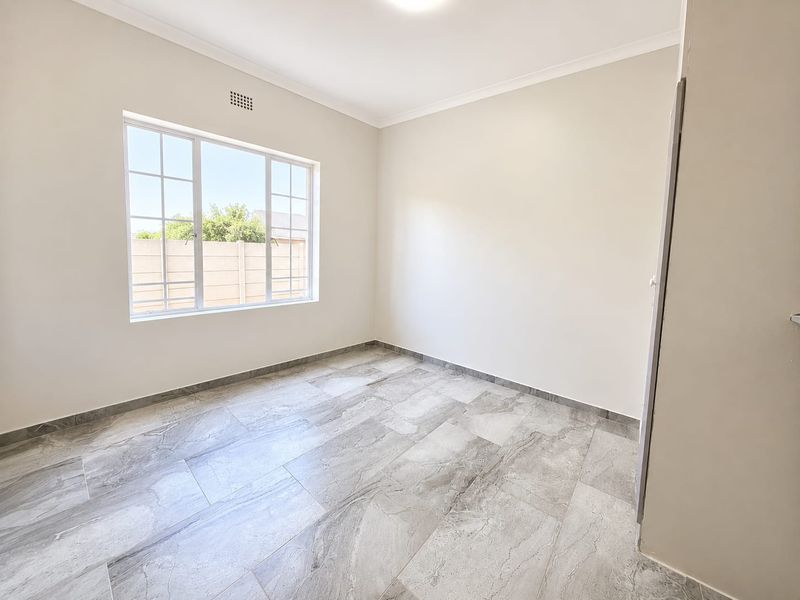 A bright, empty bedroom featuring modern grey tiled flooring, neutral walls, and a built-in cupboard, offering a clean and versatile living space.