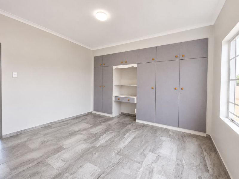 A bright, empty bedroom featuring modern grey tiled flooring and extensive built-in cabinetry with an integrated desk area.
