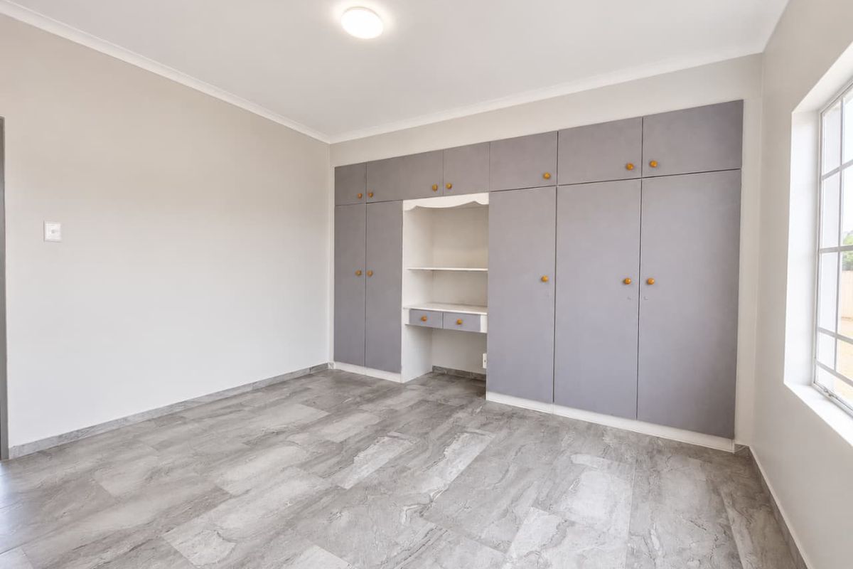A bright, empty bedroom featuring modern grey tiled flooring and extensive built-in cabinetry with an integrated desk area.