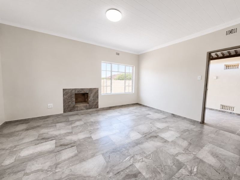 A bright, vacant living room featuring modern grey marble-look floor tiles, a built-in fireplace, and a clean white timber-look ceiling.