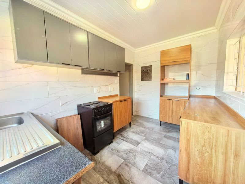 A clean, modern kitchen featuring marble-look wall tiles, wood-finish cabinetry, stone-look flooring, and a freestanding stove with ample counter space.
