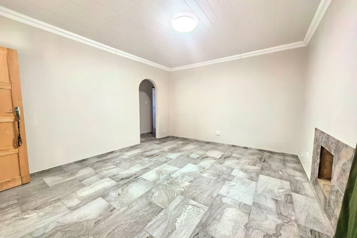 A bright, empty living room featuring large-format marble-look floor tiles, a built-in fireplace, and a classic arched doorway leading to an adjacent space.