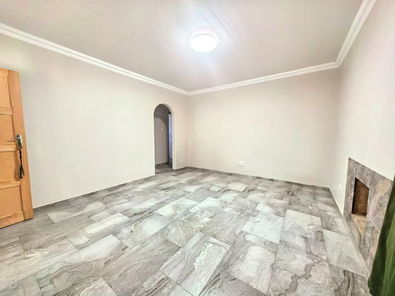 A bright, empty living room featuring large-format marble-look floor tiles, a built-in fireplace, and a classic arched doorway leading to an adjacent space.
