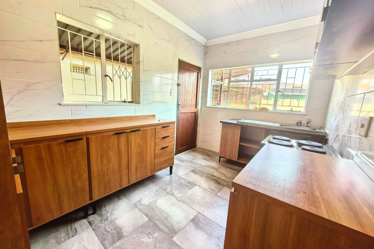 A functional kitchen featuring marble-look wall and floor tiles, built-in wooden cabinetry, an electric hob, and a stainless steel sink.