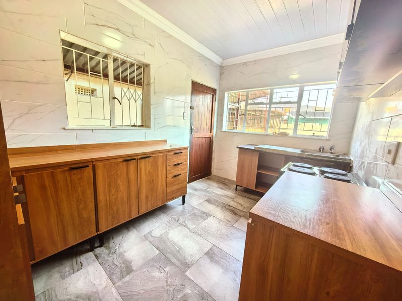 A functional kitchen featuring marble-look wall and floor tiles, built-in wooden cabinetry, an electric hob, and a stainless steel sink.