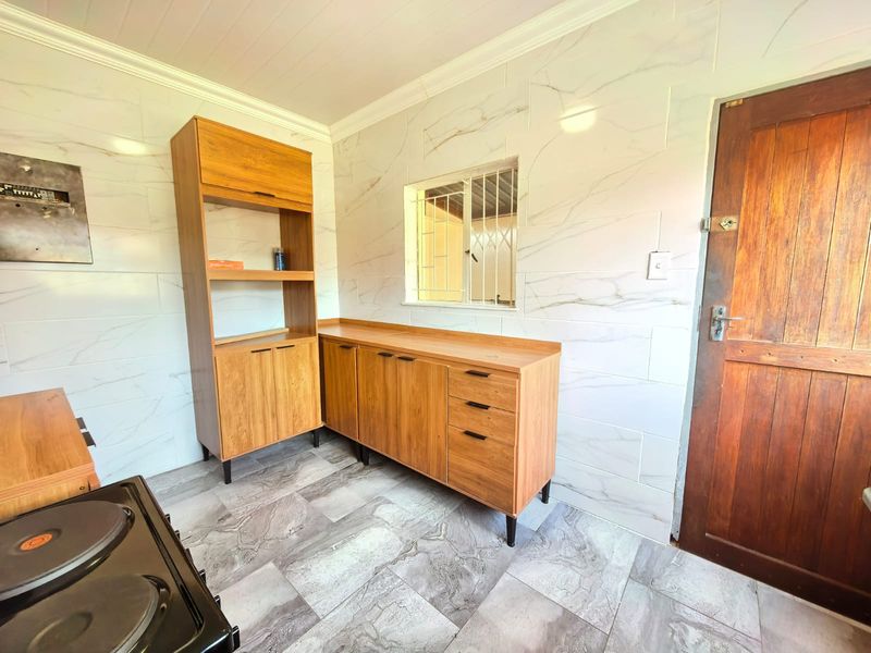 A functional kitchen area featuring modern marble-effect wall and floor tiling, built-in wooden cabinetry, and a secure timber entrance door.