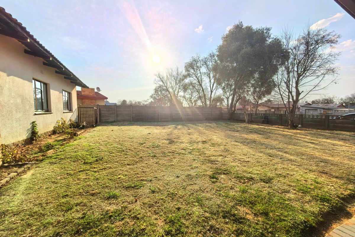 A spacious rear garden featuring a large lawn area enclosed by a precast concrete boundary wall, viewed from the side of the house.