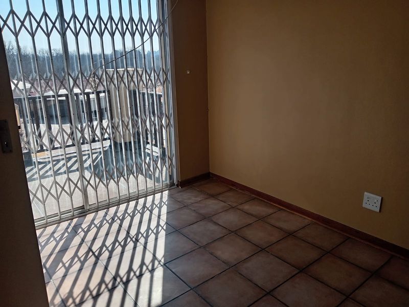 An empty living area featuring tiled flooring and a sliding glass door with a security gate, providing access to the exterior.