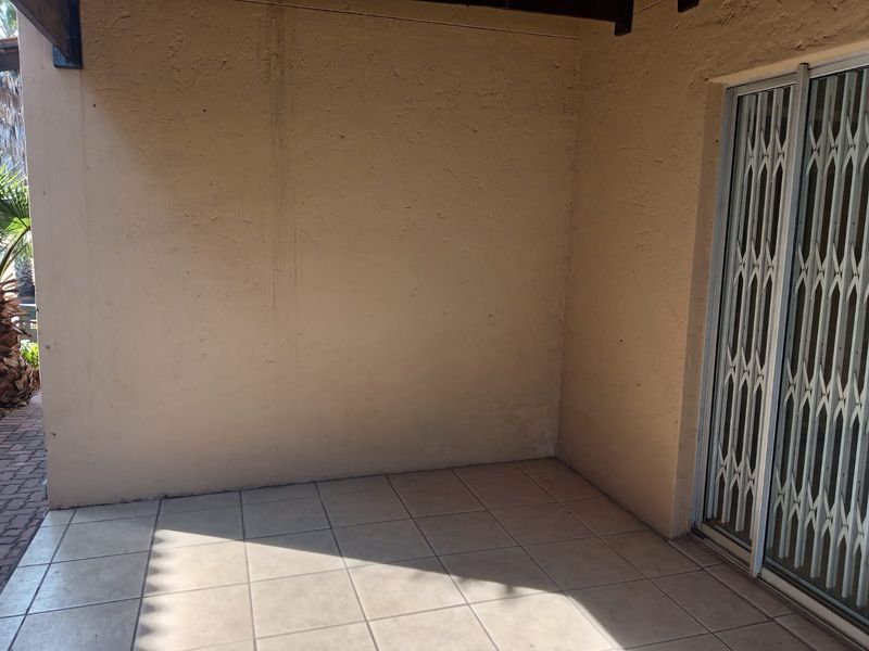 A covered patio area featuring tiled flooring and a security gate, providing a functional outdoor space with potential for enhancement.