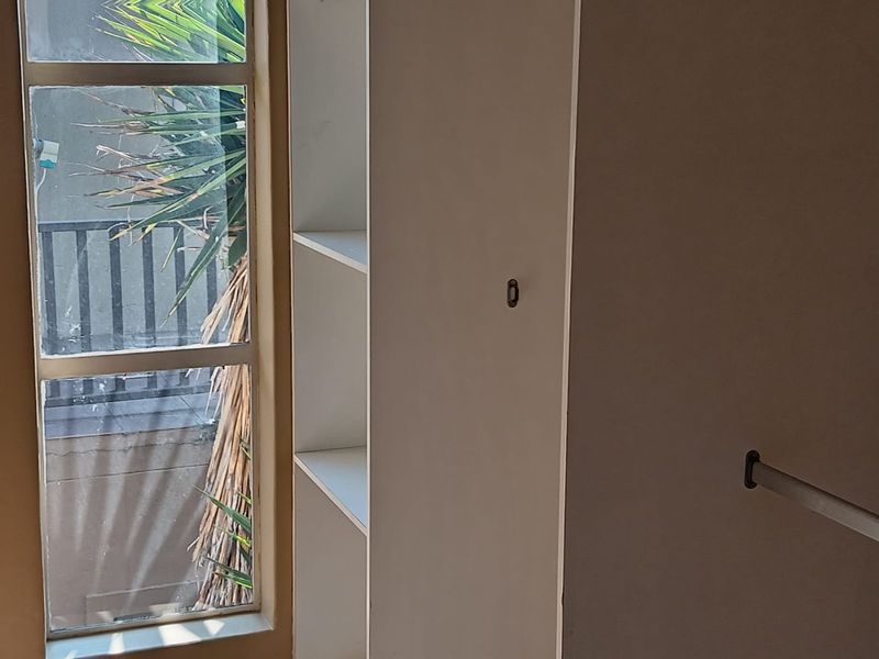 A bedroom interior featuring built-in shelving and a closet hanging rail, with natural light entering through a side window.