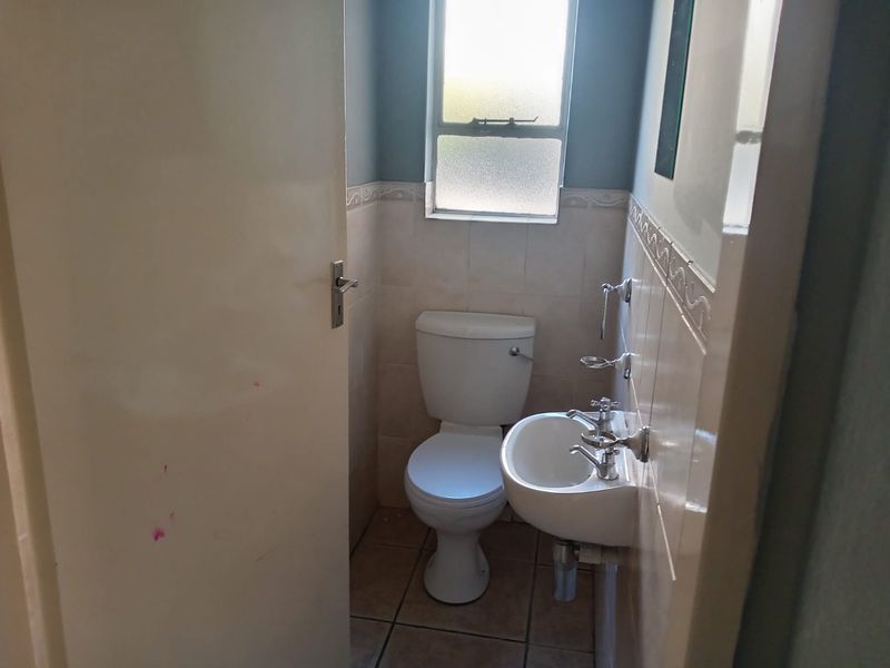 A compact guest bathroom featuring a standard toilet, wall-mounted basin, and neutral tiled finishes.