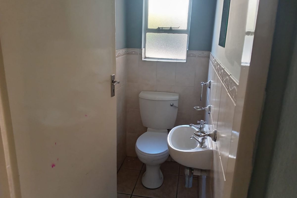 A compact guest bathroom featuring a standard toilet, wall-mounted basin, and neutral tiled finishes.