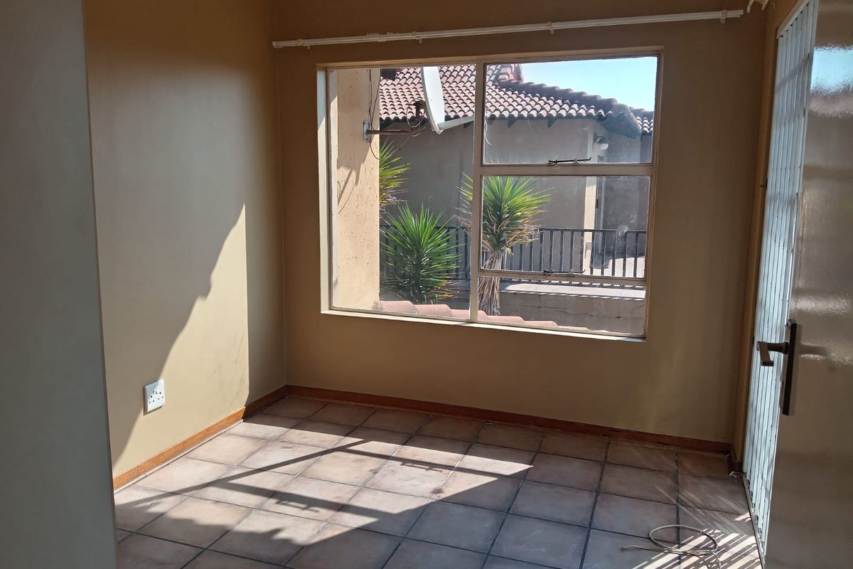 An empty bedroom featuring tiled flooring, neutral wall paint, and a large window providing natural light and views of the exterior.