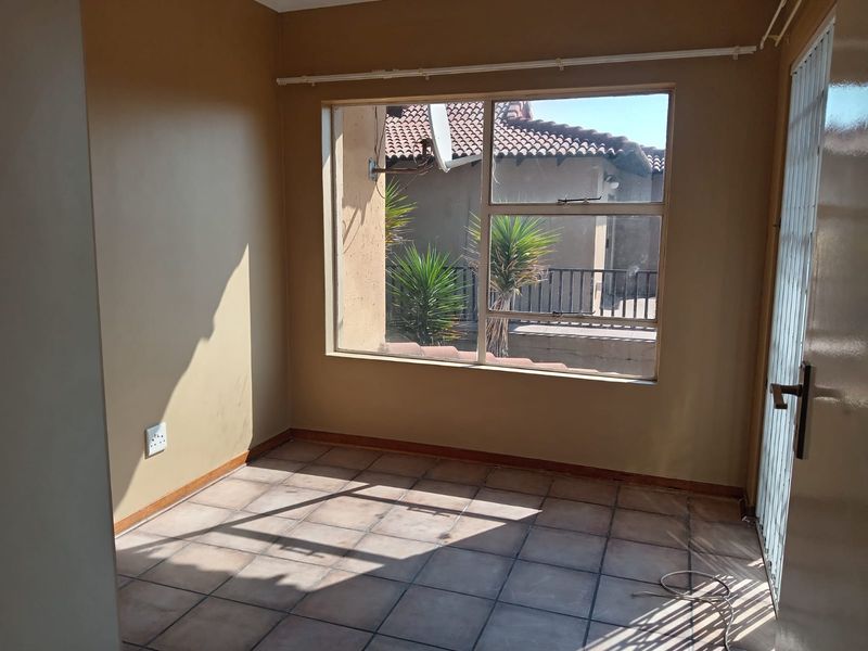 An empty bedroom featuring tiled flooring, neutral wall paint, and a large window providing natural light and views of the exterior.