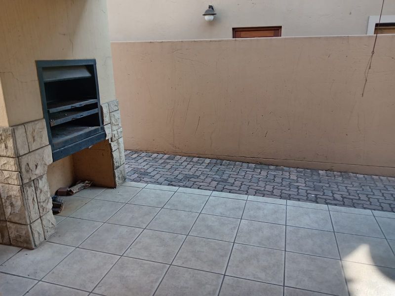 Covered patio area featuring a built-in braai, stone cladding accents, tiled flooring, and a private paved courtyard space.