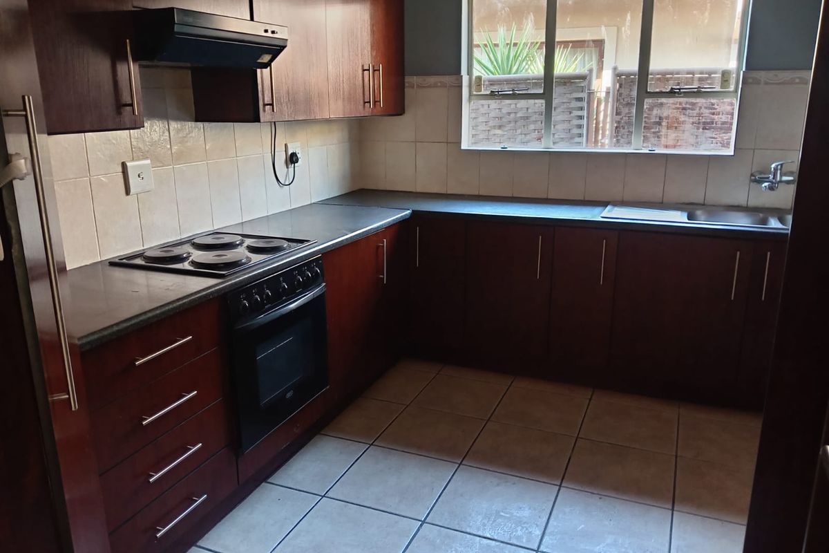 A functional kitchen featuring dark wood cabinetry, a built-in electric oven and hob, tiled splashbacks, and tiled flooring.